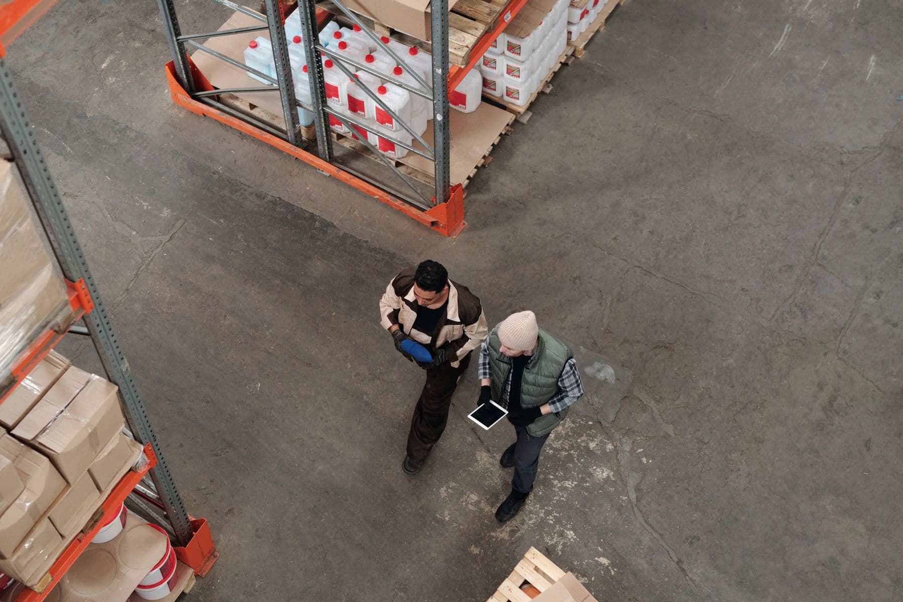 Two warehouse workers standing by shelves, one holding a tablet