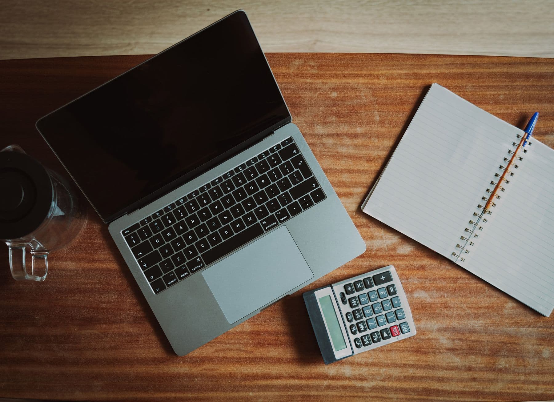 A laptop, a calculator and an open notebook on a wooden desk